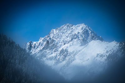 Low angle view of snowcapped mountain against blue sky