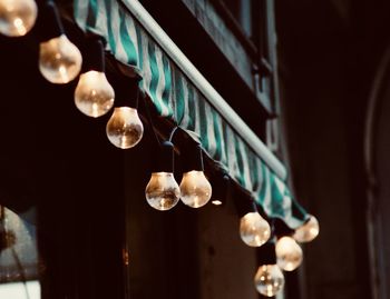 Low angle view of illuminated light bulbs hanging from window