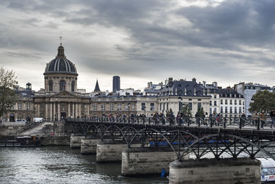 Arch bridge over river by buildings against sky in city