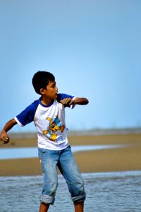 Full length of boy enjoying at beach against clear sky