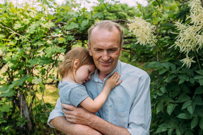 A little girl hugs her grandfather on a walk in the summer outdoors.