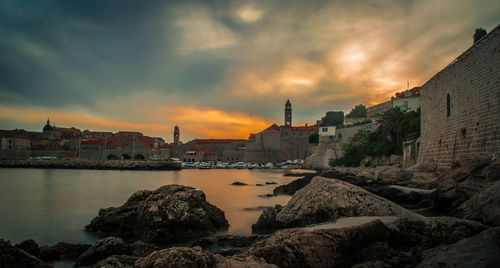 Sea by cityscape against sky during sunset