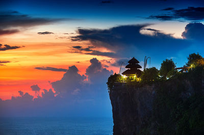 Uluwatu temple on cliff by sea against sky during sunset