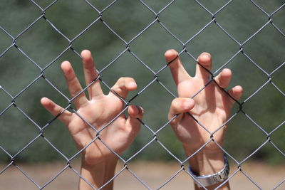 Cropped hands of person touching chainlink fence