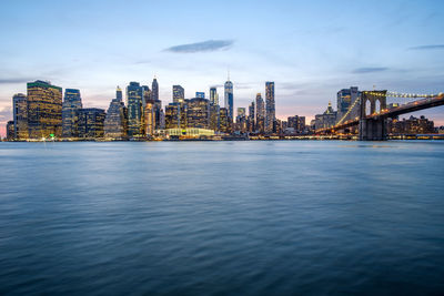 Illuminated buildings by sea against sky in city