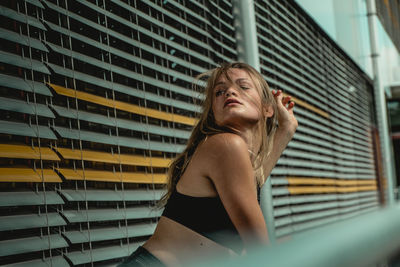 Young woman standing by blinds