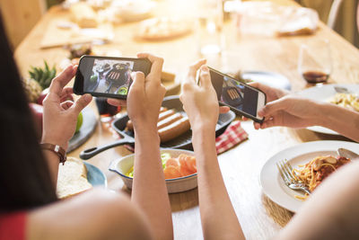 Cropped hands of women photographing food in restaurant