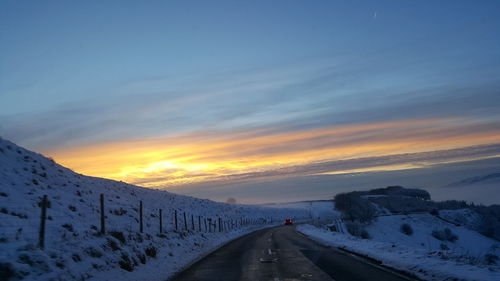 Road amidst snow covered mountains against sky during sunset