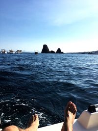 Low section of man relaxing on sea against clear sky