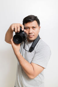 Portrait of young man photographing against white background