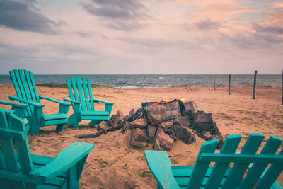 Wooden chairs on beach against sky during sunset