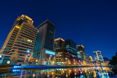 River by illuminated modern buildings against sky at night