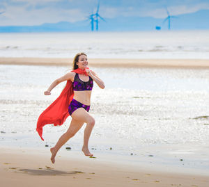 Full length of young woman wearing cape while running at beach