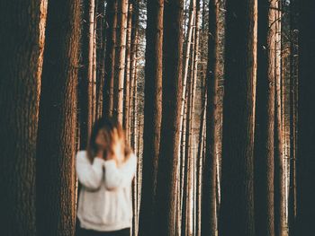 Sad woman standing against trees in forest