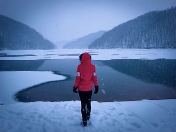 Rear view of woman with red coat standing in front of a frozen lake during winter