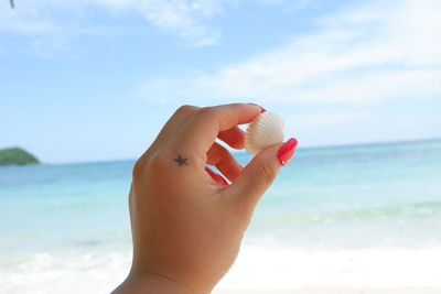 Close-up of human hand against sea and sky