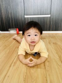 Portrait of boy sitting on wooden floor at home