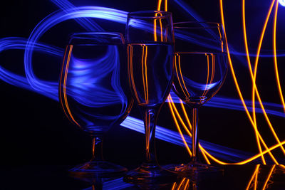 Close-up of drink in glasses on table against light in darkroom