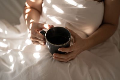 Midsection of woman holding coffee cup on bed