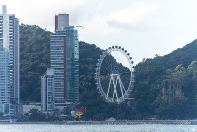 Ferris wheel by river against buildings in city