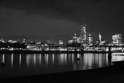 Illuminated buildings by sea against sky at night