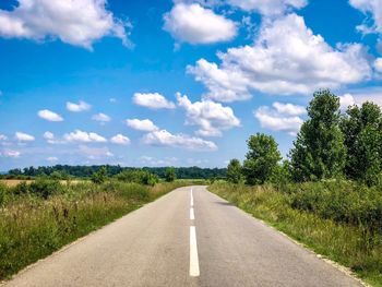 Empty road amidst field against sky