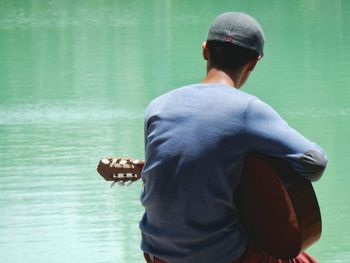 Rear view of man sitting with guitar against sea