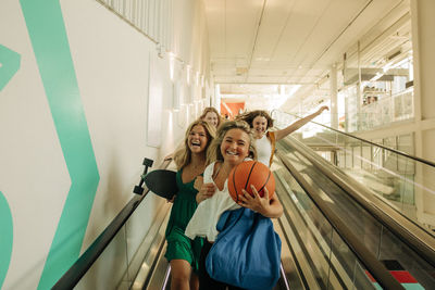 Portrait of cheerful teenage girl holding basketball enjoying with female friends in shopping mall