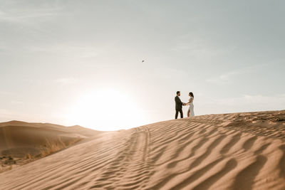 A couple in their wedding clothes on top of a desert dune at dawn. wedding concept
