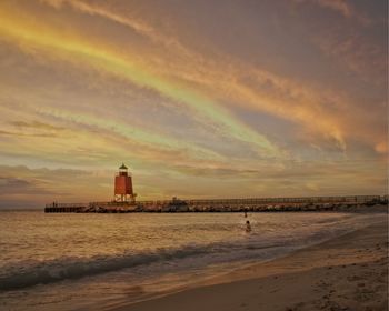 Lighthouse on beach against sky during sunset