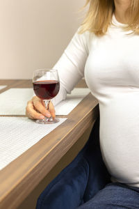 Unrecognized pregnant woman drinks a glass of alcohol free red wine, sitting in chair at kitchen