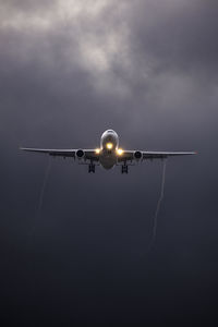 Low angle view of commercial twin engine jet airplane landing, passing through clouds.