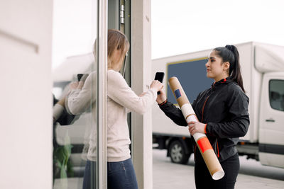 Female customer signing on smart phone while receiving package from delivery woman