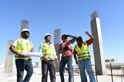 Low angle view of architects standing at construction site against clear blue sky