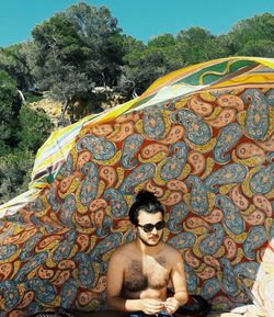Shirtless man sitting in tent on sunny day