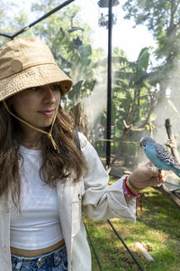Beautiful young woman feeding a bird with a wooden stick with seeds stuck to it, bird stops to eat
