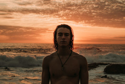 Portrait of shirtless man standing at beach during sunset