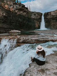 Woman sitting on rock by waterfall at crescent falls in alberta
