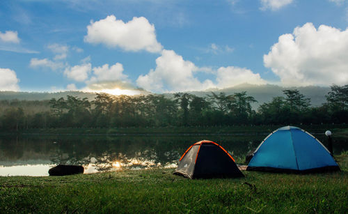 Tent on grass by lake against sky