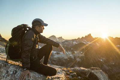 Fit active man sitting on rocky mountain ridge watching the sunset.