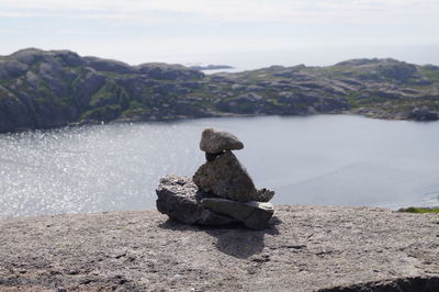 Man sitting on rock by lake against sky