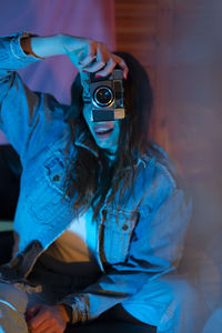 Portrait of woman holding camera against wall