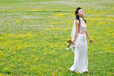Bride with closed eyes holding bouquet while standing at grassy field