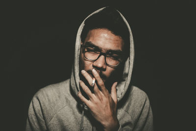 Close-up of young man smoking against black background