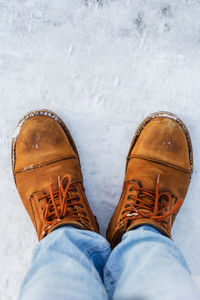 Male legs in blue jeans and brown winter boots in winter outdoors, vertical photo