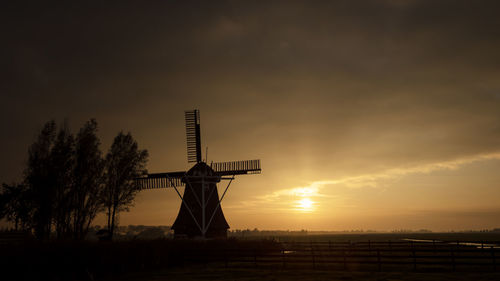 Silhouette traditional windmill on landscape against sky during sunset