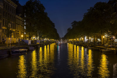 Illuminated city by river against sky at night
