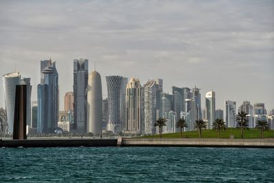Sea by modern buildings against sky in city