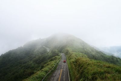 Car on road leading towards mountain against sky during foggy weather