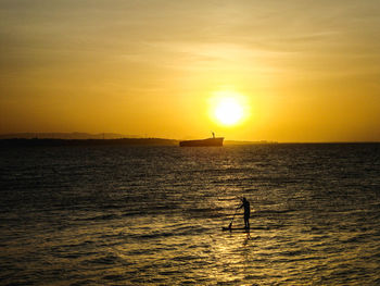 Scenic view of person paddleboarding at sunset